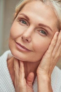 Portrait of happy beautiful middle aged caucasian woman with hands near face looking at camera and smiling during wellness procedures. Beauty, skincare and cosmetology concept