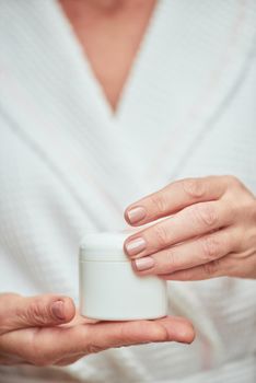 Skin care cream bottle in manicured woman hands on foreground. Beauty, skincare and cosmetology concept