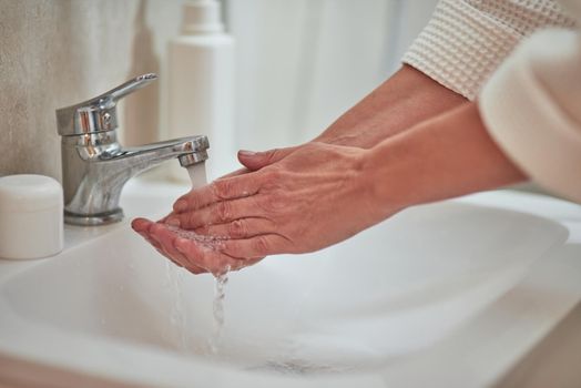 Woman washing hands with water in bathroom sink at home, close up. Beauty, skincare and cosmetology concept