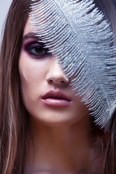 beauty brunette young girl with fashion makeup and silver feather close up on white background