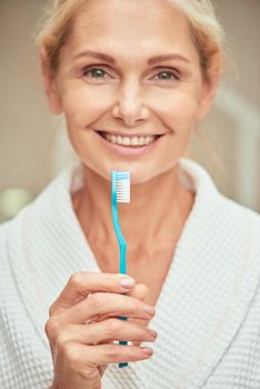 Beautiful middle aged caucasian woman with toothbrush in hand smiling at camera, selective focus. Beauty, skincare and cosmetology concept