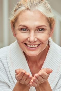 Portrait of happy middle aged caucasian woman with open palms looking at camera and smiling during wellness procedures. Beauty, skincare and cosmetology concept