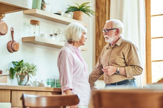 Elderly husband and wife talking and looking at each other while enjoying morning at home. Family and relationships concept