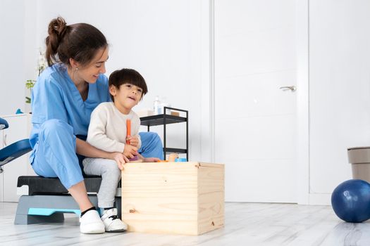 Therapist doing development activities with a little boy with cerebral palsy, having rehabilitation, learning . Training in medical care center. High quality photo.