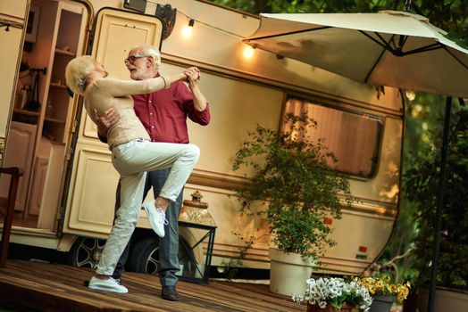 Full length photo of happy senior couple dancing while staying on the van porch evening. Travel concept