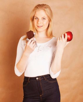 young beauty blond teenage girl eating chocolate smiling, choice between sweet and red apple
