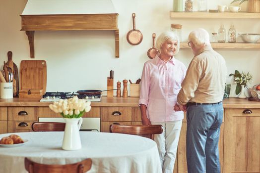 Happy senior wife looking at her husband while talking together at their cozy house. Family and relationships concept