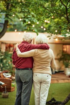 Back view of senior married couple looking at their campervan and hugging while standing outdoors. Travel concept