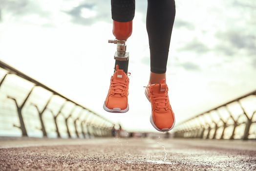 Never give up Cropped photo of disabled woman with prosthetic leg in sportswear jumping on the bridge. Disabled sport concept. Motivation