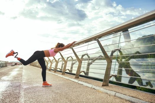 Morning workout. Disabled athletic woman with prosthetic leg in sportswear doing sport exercises while standing on the bridge. Side view. Disabled sport concept. Motivation