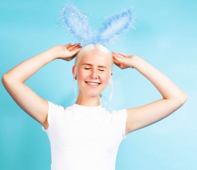 young pretty blond girl with rabbit ears posing cheerful on blue background, lifestyle people concept close up