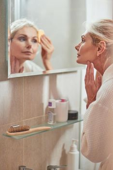 Mirror reflection of smiling middle aged caucasian woman using collagen anti aging under eye patches. Beauty, skincare and cosmetology concept