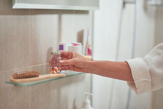 Wellness vitamins bottle on shelf in bathroom held by woman hand. Beauty and cosmetology concept