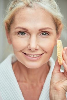 Spa middle aged caucasian woman with clean shiny skin holding facial sponge while smiling at camera. Beauty, skincare and cosmetology concept