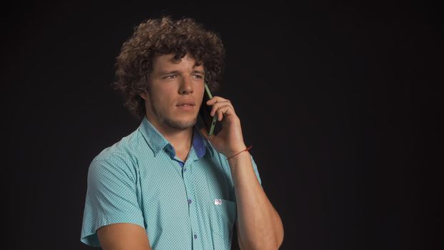 Serious young man speaks on mobile phone. Cut out on black background.