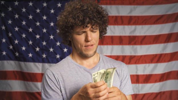 Successful American man counts money. Handsome businessman holds pack of 100 dollar bills against background of USA flag. Happy winner concept.