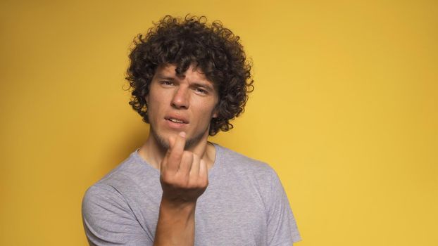 Romantic young man shows korean love sign. Shaggy guy folded two fingers together like mini heart looking into the camera. Cut out on white background.