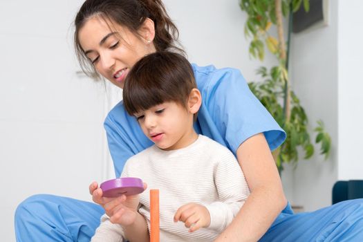 Therapist doing development activities with a little boy with cerebral palsy, having rehabilitation, learning . Training in medical care center. High quality photo.