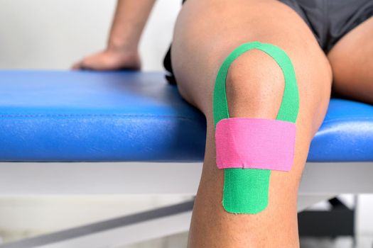 Young sportive male athlete treating injured knee with kinesio tape. Close up. Kinesiology, physical therapy, rehabilitation concept. High quality photo