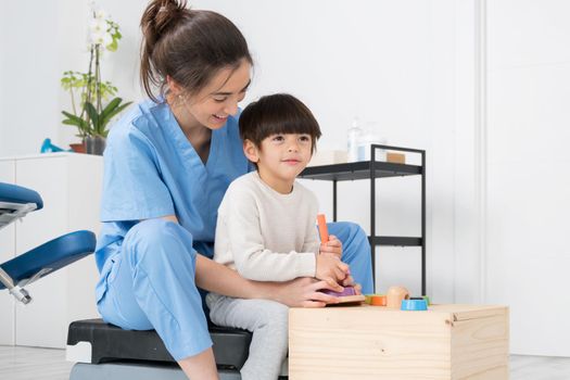 Therapist doing development activities with a little boy with cerebral palsy, having rehabilitation, learning . Training in medical care center. High quality photo.