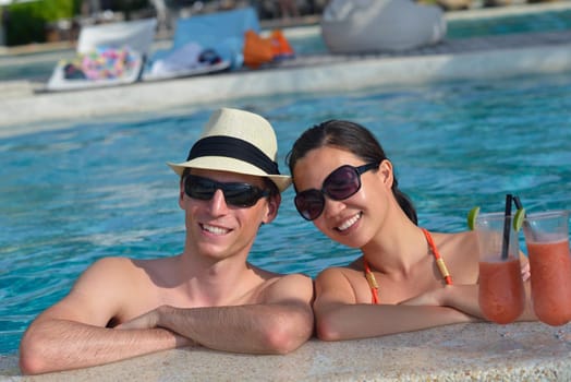 happy young couple relax and take fresh drink at summer vacation on swimmin pool