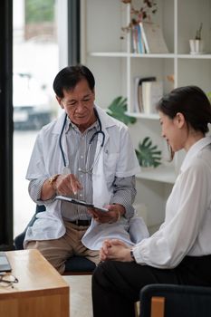 Senior asian doctor physician consulting young female patient, talking to client at medical checkup visit. Geriatric diseases treatment. Elderly medical health care concept