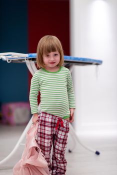 portrait of a cute little girl with a pink dress in her hand that she wants to put on herself at stylish apartment