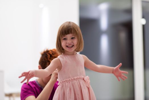 family having fun on beutiful evening at home young mother helping cute little daughter while putting on a pink dress for dancing at home