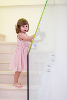 happy cute little girl in pink dress enjoying while playing on wooden stairs at stylish two level apartment