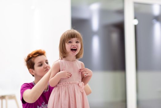 family having fun on beutiful evening at home young mother helping cute little daughter while putting on a pink dress for dancing at home