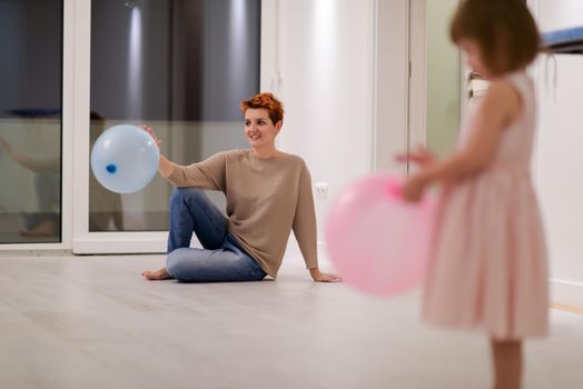 happy family spending time together young redhead mother and cute little daughter having fun while playing with balloons near the window on beautiful evening at home