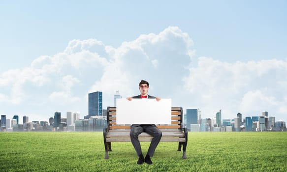 Young businessman sits on a wooden bench and holds a large white banner