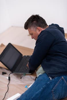 man checking business workflow using laptop computer while lying on floor with cardboard box placed below him during renovation of the apartment