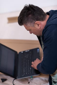 man checking business workflow using laptop computer while lying on floor with cardboard box placed below him during renovation of the apartment