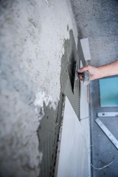 experienced senior construction worker installing big ceramic tiles on interior concrete walls