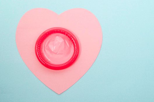 Pink condom unpackage on pink paper heart shape with copy space for your text or message.