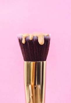 pouring liquid beige makeup foundation on a brush makeup with pink background.