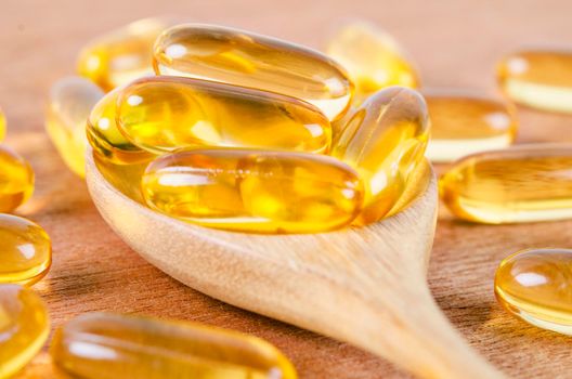 Cod liver oil omega 3 gel capsules on a spoon on wooden background. Fish oil vitamins.