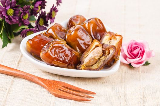 Dried dates fruit in white bowl and wooden fork.