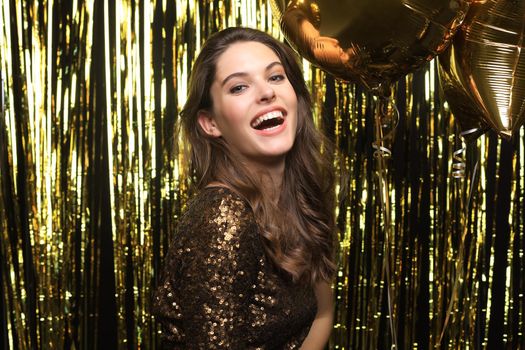 Happy woman in festive outfit holding gold balloons