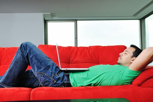 young man relax on red sofa and work on laptop at home indoor 