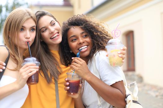 Three trendy cool hipster girls, friends drink cocktail in urban city background
