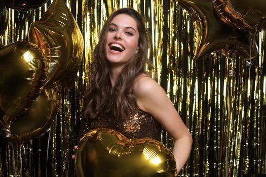 Happy woman in festive outfit holding gold balloons