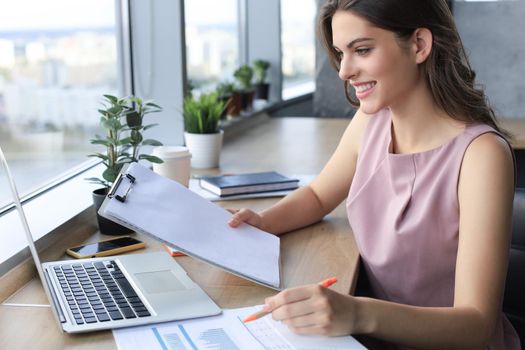 Beautiful young woman writing something down while sitting in modern office