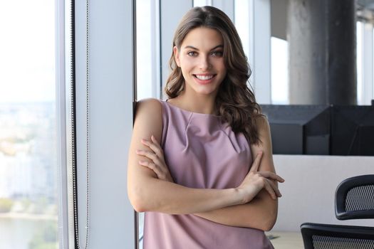 Attractive business woman looking at camera and smiling while standing in the office near the window.