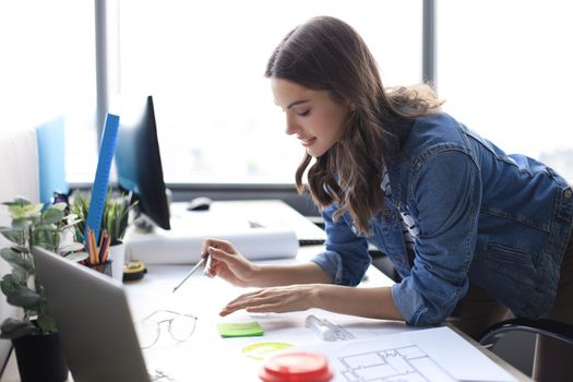 Young architect drawing with a compass on blueprint and smiling while working in the creative office