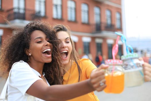 Trendy cool hipster girls, friends drink cocktail in urban city background