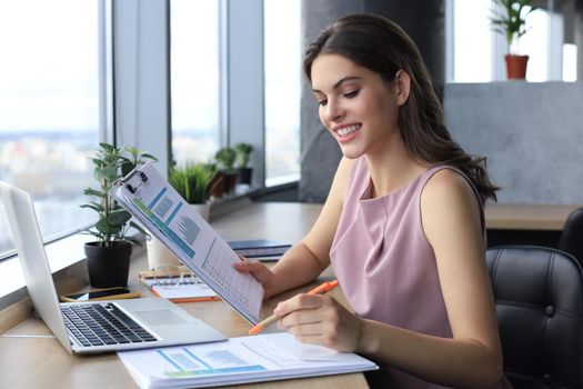 Beautiful young woman writing something down while sitting in modern office