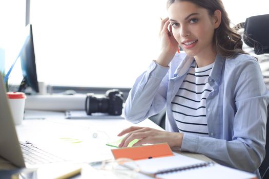 Beautiful business woman is writing something down while sitting in the office desk.