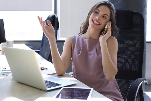 Attractive business woman talking with collegues on the mobile phone while sitting in the office desk.